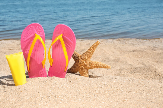 Stylish flip flops, sun protection cream and starfish on sandy beach, space for text