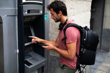 Young man withdrawing money from credit card. Man typing pin code on keypad of ATM mashine.