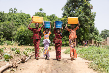 Group of four strong beautifully dressed black African girls carrying water containers on their...