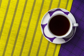 Top view of a cup of coffee on a yellow and purple surface