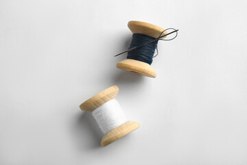 Colorful sewing threads with needle on white background, top view