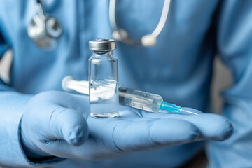 Male, doctor in blue shirt and gloves, holding in the hand a syringe and vaccine bottle against disease coronavirus or flu, vaccination concept