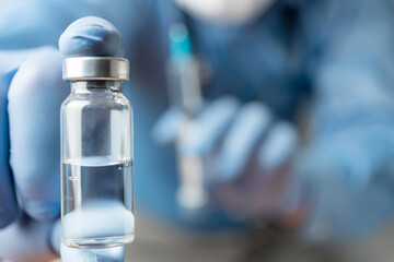 Male, doctor in blue shirt and gloves, holding in the hand vaccine bottle against disease coronavirus or flu, vaccination concept