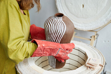 Female ceramist takes out from a kiln after firing. Master ceramist working in pottery studio....