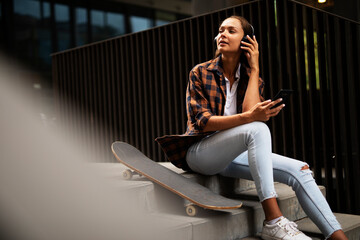 Fashion woman with skateboard. Urban brunette woman listening the music