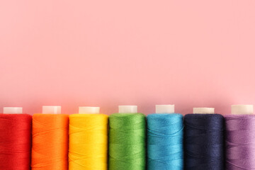 Different colorful sewing threads on pink background, flat lay. Space for text