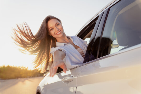 Photo portrait smiling woman riding in car wearing white casual shirt with flying on wind hair keeping hand forward