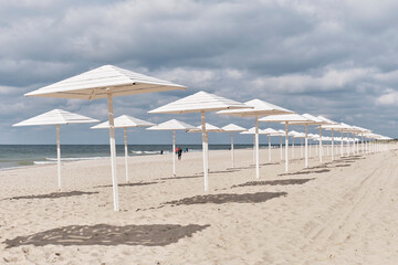 Baltic sandy beach with white wooden sun umbrellas in autumn. Seaside landscape