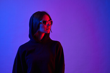 Girl with long hair and sunglasses in a white shirt poses in neon light in the studio.