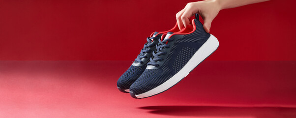 Hand hold sports shoes on red background. Holding new fashion sneakers for running. Choosing and...