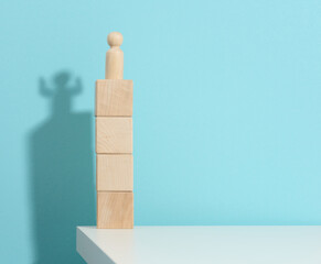 wooden figurine of a man stands high on the cubes, the shadow of a strong and victorious. Everyone is stronger than he thinks, a superhero. Blue background