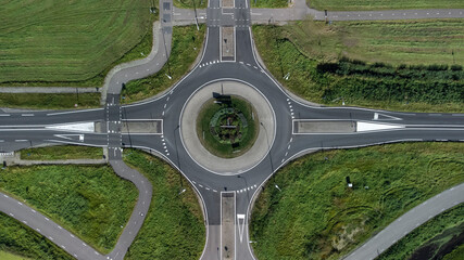 Aerial view of a small roundabout at the intersection of two asphalted gray country roads © Tjeerd
