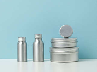empty silver metal bottle for cosmetics on white table, blue background. Packaging for cream, gel, serum, advertising and product promotion. Mock up