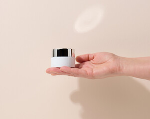 female hand holds empty white jar for cosmetics. Packaging for cream, gel, serum, advertising and product promotion, mock up