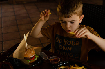 a boy eats potatoes and a hamburger in a cafe