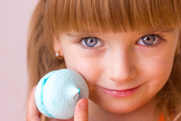 Beautiful little girl holding a blue sweet dessert macarons meringue in her hands portrait close-up, sweet pastries happy childhood childish emotions, selective focus	