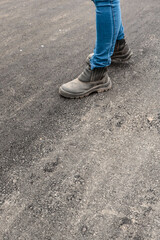 Foot of an unidentified person, wearing jeans and wearing a very worn and dusty boot, on a paved floor
