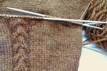 Knitting on knitting needles. Brown woolen fabric with cables pattern on knitting needles