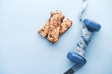 dumbbell, measurement tape and oat protein bars on table 