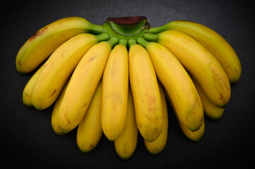 Fototapeta na wymiar Ripe and natural looking small bananas on dark background.