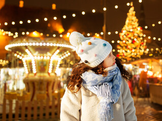 winter holidays and children concept - portrait of little girl over christmas market or amusement...