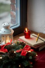 winter holidays, new year and decorations concept - christmas fir wreath, books, candle and lantern on window sill at home