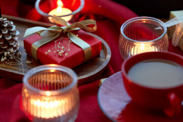 holidays, decoration and celebration concept - close up of christmas gift, cup of coffee and candles on red tablecloth on window sill at home