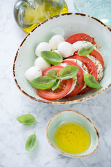 Caprese salad with mozzarella, red tomatoes and green basil leaves served in a green bowl, vertical shot, selective focus, close-up