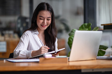 Fototapeta premium Shot of an Asian young business Female working on laptop computer in her workstation.Portrait of Business people employee freelance online report marketing e-commerce telemarketing concept.