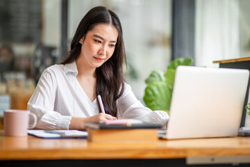 Shot of an Asian young business Female working on laptop computer in her workstation.Portrait of Business people employee freelance online report marketing e-commerce telemarketing concept.