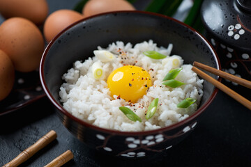 Close-up of tamago kake gohan or japanese warm rice mixed with a raw chicken egg and served in a black bowl, studio shot