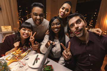 holidays, friendship and celebration concept - multiethnic group of happy friends having christmas dinner at home and taking selfie