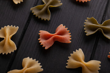 Dry farfalle tricolore pasta pattern. Uncooked Macaroni. Heap of raw traditional italian pasta on a wooden table.