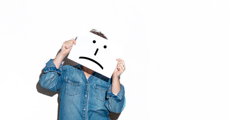 Person holding a paper on his face with a sad emoji drawn on it isolated on a white background