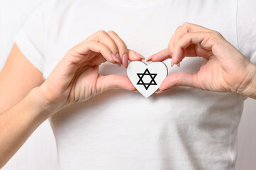 The girl holds a small heart with a symbol of Judaism on her chest. The concept of the Jewish religion. Close-up