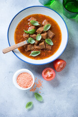 Plate of tomato soup with lentils and croutons, above view on a light-blue stone background, vertical shot