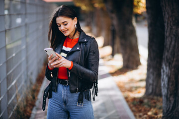 Young trendy woman in leather jacket using phone