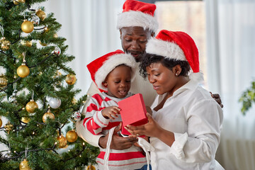 family, winter holidays and people concept - happy african american mother, father and little son opening gift box at home on christmas