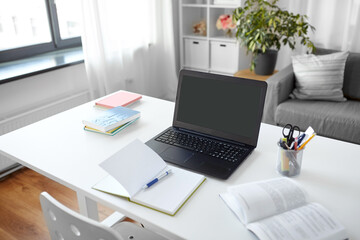 interior, education and business concept - open laptop computer, notebook and book on table at home...