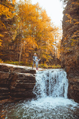 Fototapeta premium young woman with toddler girl looking at waterfall at autumn forest