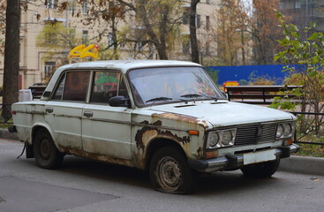An old rusty white Soviet passenger car in the courtyard of a residential building, Zanevsky...
