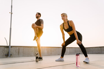 Young man and woman doing exercise while working out together on parking