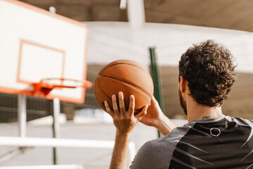 Young brunette man playing basketball on parking