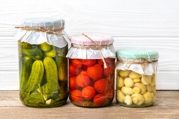 Homemade pickled cherry tomatoes, cucumbers, champignons, garlic, eggplant, red peppers in jars on wooden shelf Homemade canned and fermented foods concept Seasonal product