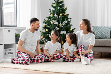 family, winter holidays and people concept - happy mother, father and two daughters sitting under christmas tree at home