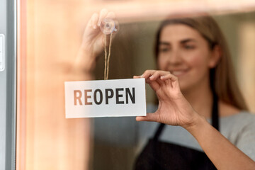 small business, reopening and service concept - happy smiling woman hanging reopen banner on window or door glass