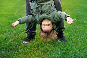 Father playing with little son outdoors on a grass. Toddler boy swinging upside down. Happy child...