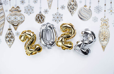 Fototapeta na wymiar Banner. Happy New Year and Merry Christmas. Balloons made of gold and silver foil with the number 2022, snowflakes, garland and Christmas tree balls on a white background. Flat lay.