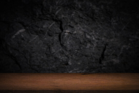 Free space on a wooden table for displaying products with a blurred black wall background.	