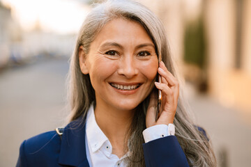 Mature asian woman with grey hair smiling and talking on mobile phone